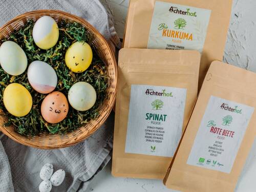 Gefärbte Eier in Osternest, daneben drei Packungen Färbepulver von Achterhof
