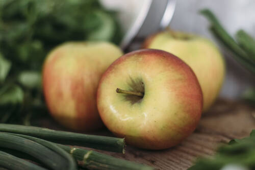Äpfel neben anderem Herbstgemüse auf einem Holzbrett.