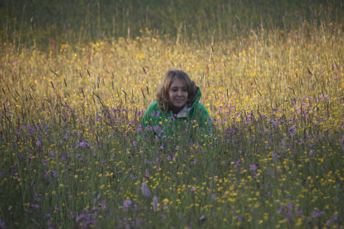 Allgäuer Wildkräuterführerin Ina Tenhündfeld kniet in einer üppigen Wiese