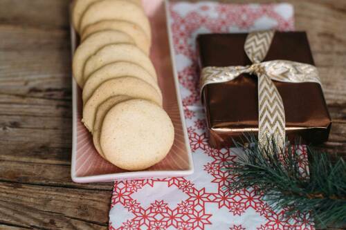 Vegetarische Anisplätzchen neben Geschenk und Tannenzweig auf Holz.