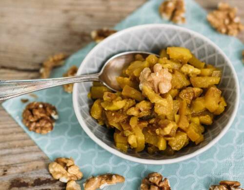 Apfel-Walnuss-Chutney in grauer Schüssel mit Löffel von oben fotografiert vor blauem Hintergrund.