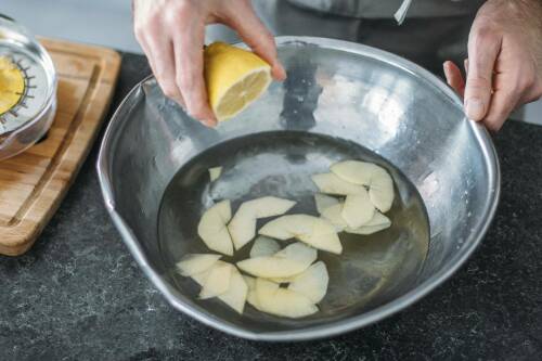 Apfelscheiben in Wasser mit Hand und Zitrone vor hellem Hintergrund.