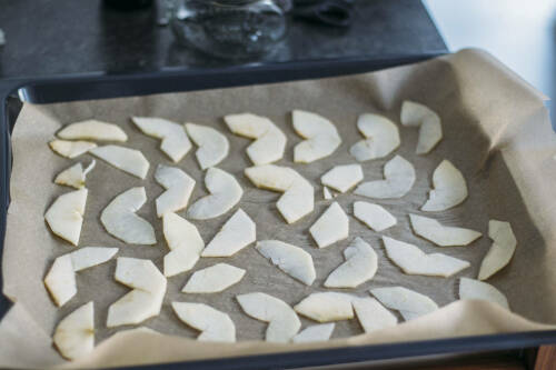 Apfelringe auf Backblech vor dunklem Hintergrund.