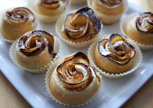 Apfelrosen in Muffin-Förmchen auf einem Teller, knusprig gebacken. Von oben fotografiert.