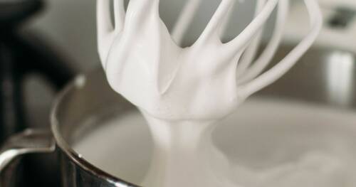 Aufgeschlagener Eischnee aus Kichererbsenwasser im Behälter einer Küchenmaschine. Von der Seite fotografiert.