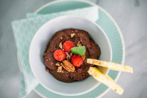 Avocado Schokocreme in Schüssel mit Himbeeren vor hellem Hintergrund.