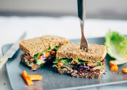 Buntes Sandwich mit sommerlicher Note auf einer grauen Platte angerichtet und von vorne fotografiert.