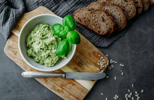 Basilikum-Sonnenblumenkern-Aufstrich in einer Schüssel mit aufgeschnittenem Brot
