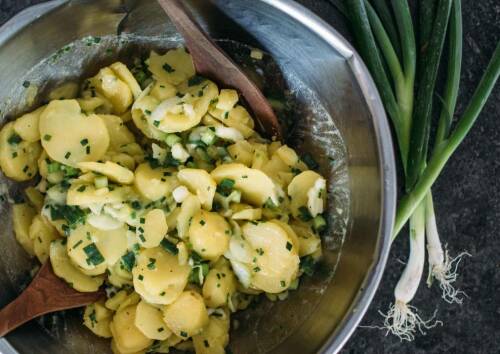 Bayerischer Kartoffelsalat in einer großen Blechschüssel mit Essig, Öl und Gemüsebrühe angemacht. Von oben fotografiert.