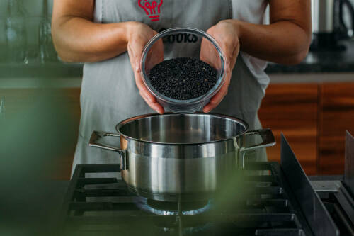 Belugalinsen in Schüssel und Händen über Topf in Küche.