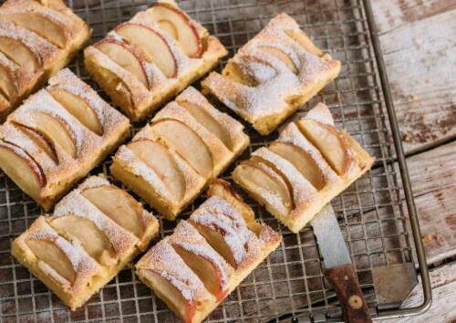 Apfelkuchen vom Blech in Stücke geschnitten, mit Puderzucker darauf. Auf einem Gitter drapiert und von oben fotografiert.