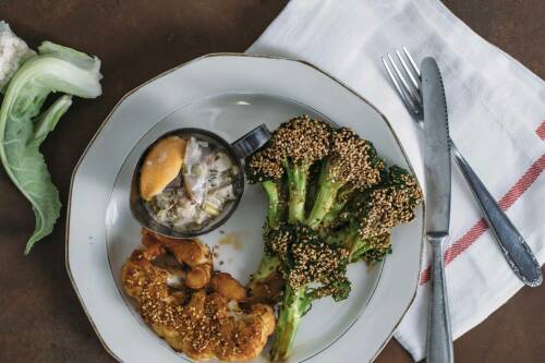 Blumenkohl- und Brokkolisteaks neben Ei auf weißem Teller vor dunklem Hintergrund.