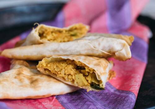 Mit Blumenkohlreis gefüllte Teigtaschen auf einem pink-lila Tuch, von der Seite fotografiert.