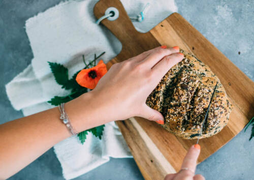 Laib Brennnesselbrot auf einem Holzbrett. Das Foto zeigt, wie es gerade in Scheiben geschnitten wird, von oben fotografiert.