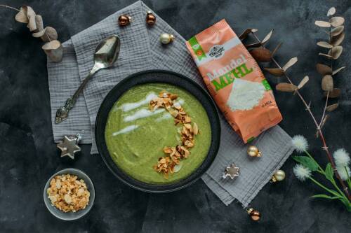 Kräftig-grüne Brokkoli-Mandel-Cremesuppe in einer schwarzen Schale, daneben Mandelmehl-Packung von Bauckhof