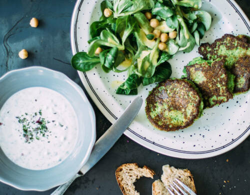 Brokkoli- Parmesan- Bratlinge mit Feldsalat und Dressing vor dunklem Hintergrund.