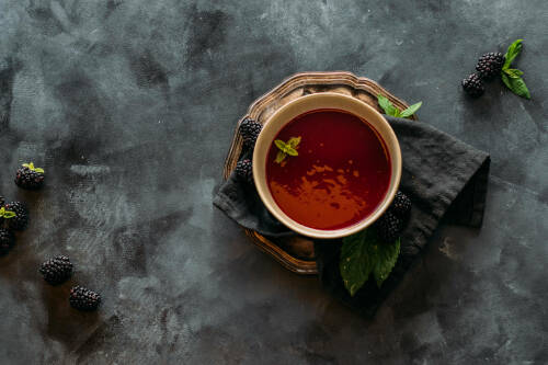 Brombeerdressing in Schüssel auf Goldteller neben Brombeeren vor dunklem Hintergrund.