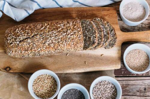 Buchweizen-Dinkel-Kastenbrot mit Körnern auf Schneidebrett vor hellem Hintergrund.