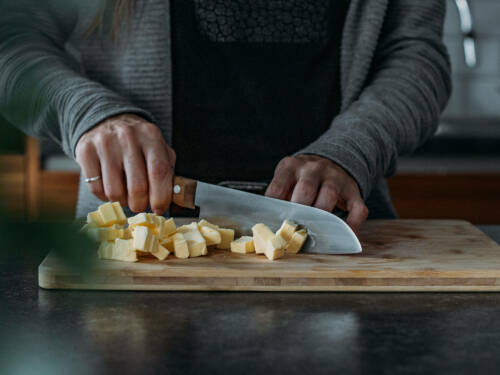 Butter kleinmachen auf Schneidebrett vor dunklem Hintergrund.
