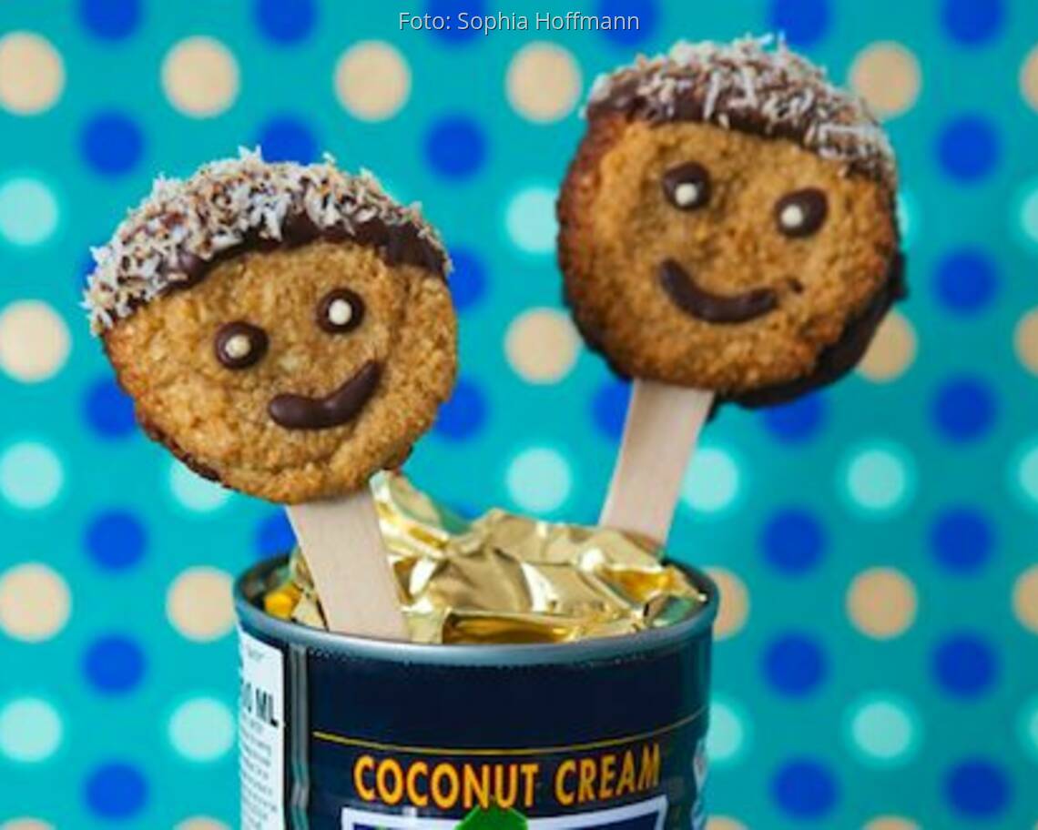 Smiley-Kekse auf Holzstäbchen in eine Dose gesteckt vor blauer Pünktchentapete