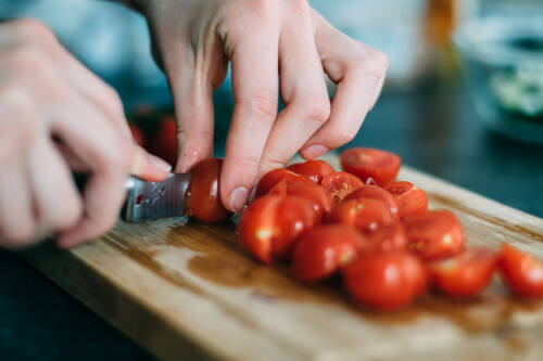 Cherrytomaten schneiden auf Schneidebrett vor dunklem Hintergrund.