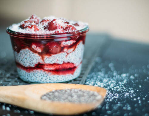 Chiapudding mit Vanillekirschen und Holzlöffel vor dunklem Hintergrund.