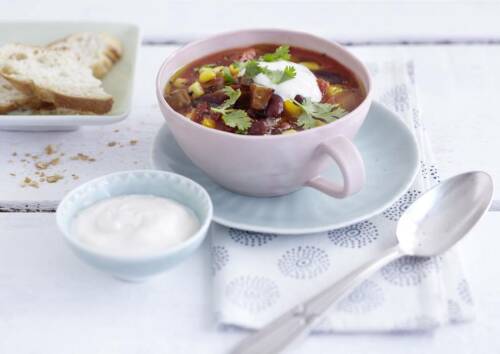 Fleischloses Chili in einer Tasse, Joghurt-Dip und Löffel daneben, dazu Brot, von vorne fotografiert