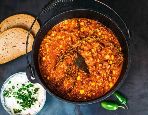 Chili mit Tofu sin Carne und zwei Scheiben Brot in Topf vor dunklem Hintergrund.