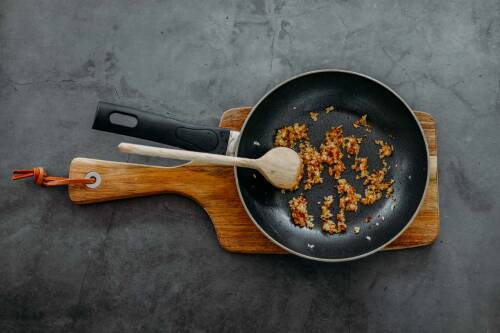 Schalotten in Pfanne angeschwitzt vor dunklem Hintergrund.