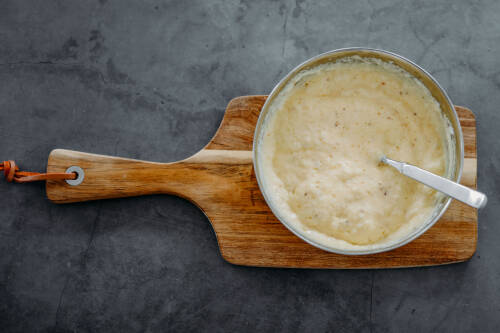 Eischnee mit Knoblauch in Topf auf Schneidebrett vor dunklem Hintergrund.