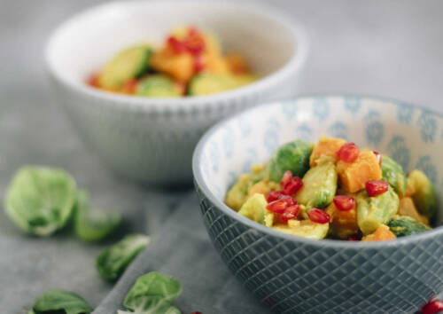 Exotisches Curry mit Rosenkohl und Süßkartoffel in kleinen Schalen, daneben Rosenkohlblätter. Von der Seite fotografiert.