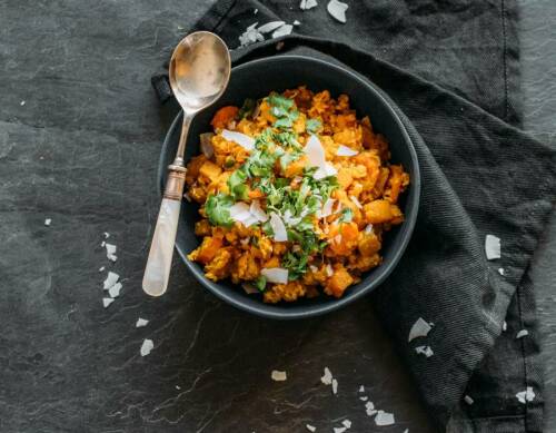 Curry mit Steckrübe in schwarzem Teller mit Esslöffel vor schwarzem Hintergrund.