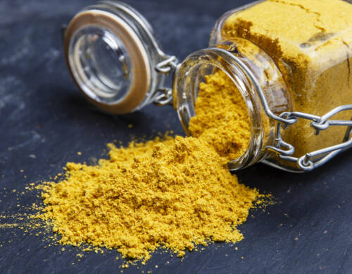 Currypulver in Glas vor dunklem Hintergrund.