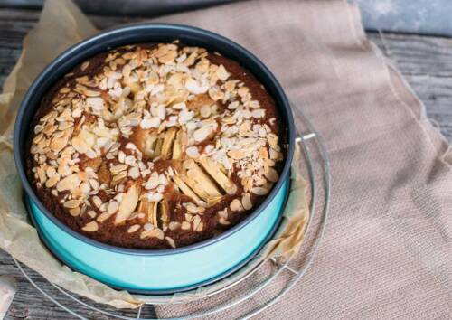 Einfacher, gedeckter Apfelkuchen mit Mandelblättchen bestreut in einer türkisen Springform auf einem Gitter. Von oben fotografiert.