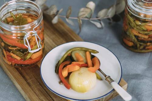 Eingelegtes Gemüse in Weckglas und Teller vor hellem Hintergrund. 