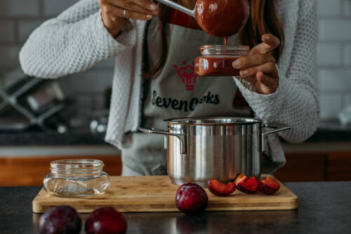 Selbstgemachtes Pflaumenmus wird mit einer Suppenkelle vom Topf in Gläser gefüllt.