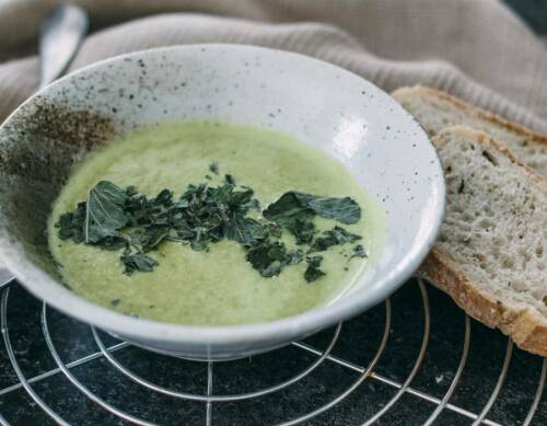 Erbsensuppe neben aufgeschnittenem Brot vor hellem Hintergrund.
