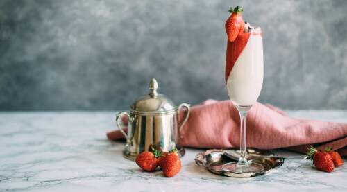 Sektglas gefüllt mit Cashew Panna Cotta und Erdbeer-Mousse vor hellgrauem Hintergund, von vorne fotografiert.