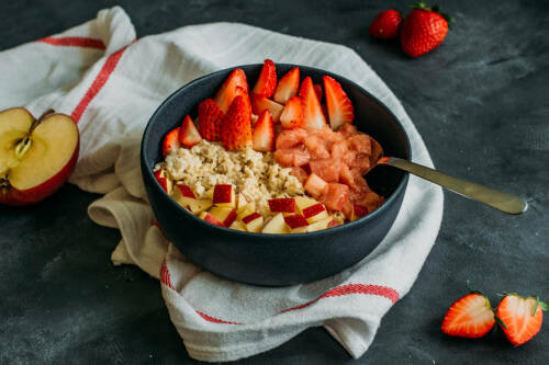 Erdbeer-Rhabarber-Porridge in Schüssel vor dunklem Hintergrund.
