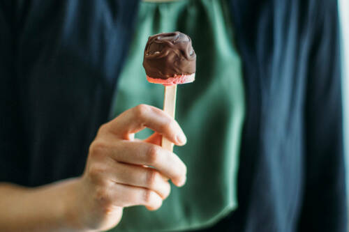 Erdbeer-Schoki-Cakepop in Hand vor grünem Hintergrund.