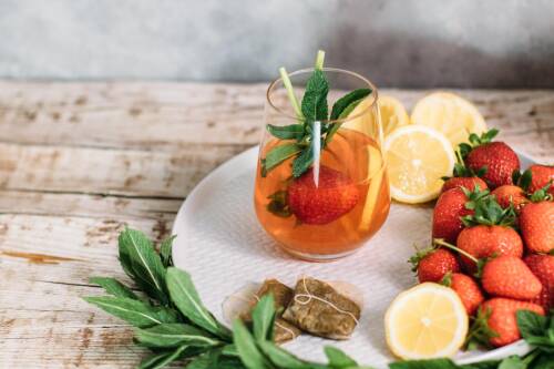 Glas Eistee auf einem Teller mit frischem Obst: Zitronen und Erdbeeren von vorne fotografiert