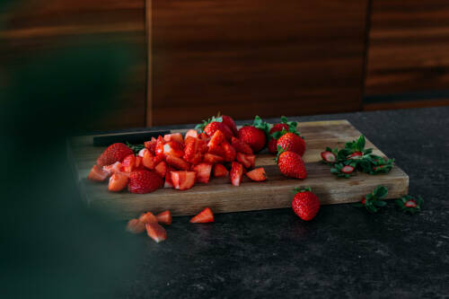 Erdbeeren geschnitten auf Schneidebrett vor dunklem Hintergrund.