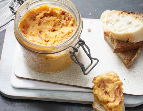 Erdnuss-Süßkartoffel-Aufstrich in Weckglas mit Baguettescheiben vor hellem Hintergrund.