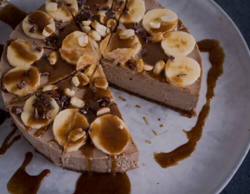 Erdnussbutter Torte mit Bananen und Schokoguss vor hellem Hintergrund.