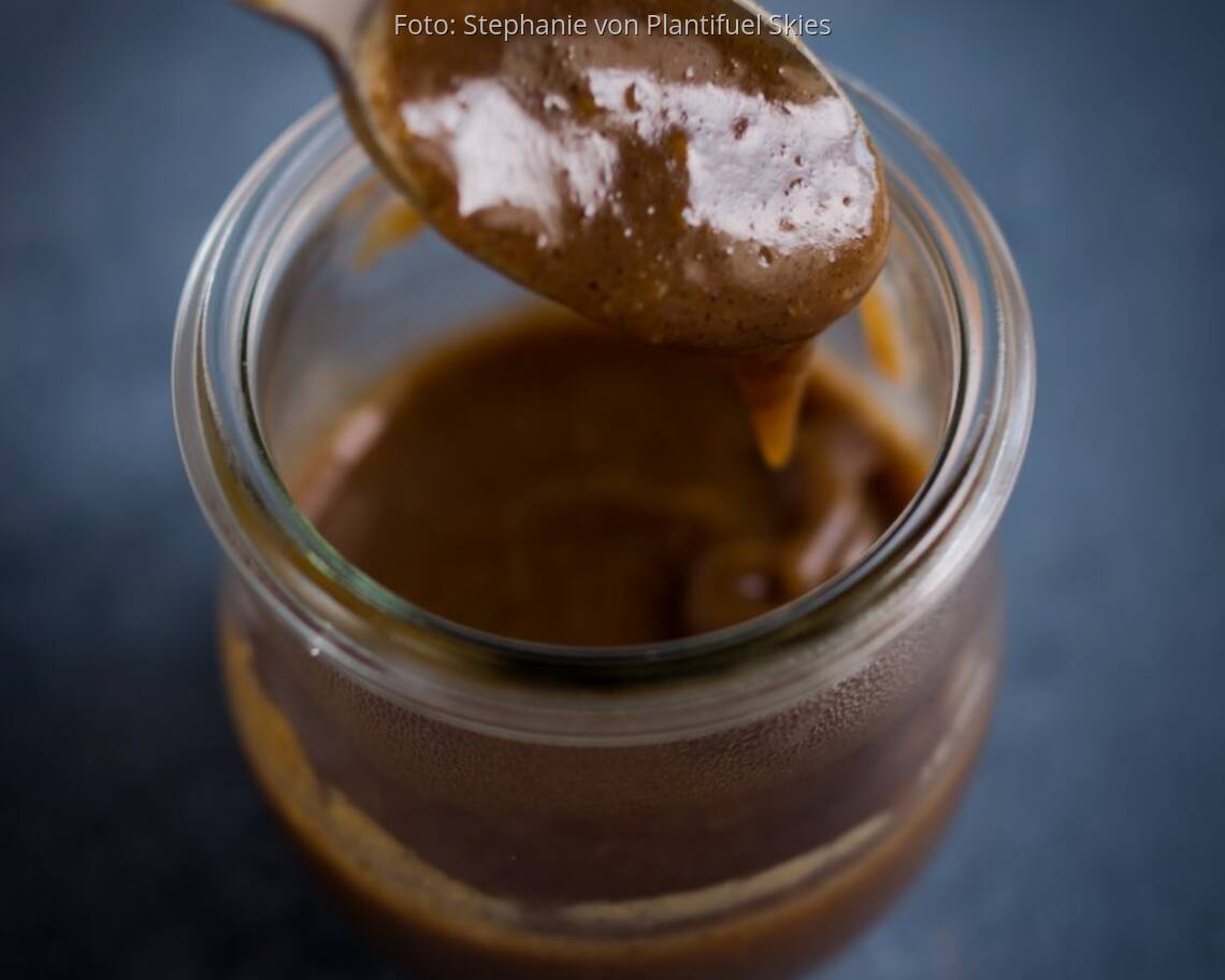 Glas mit selbstgemachter Erdnuss-Karamell-Sauce auf dunkler Platte