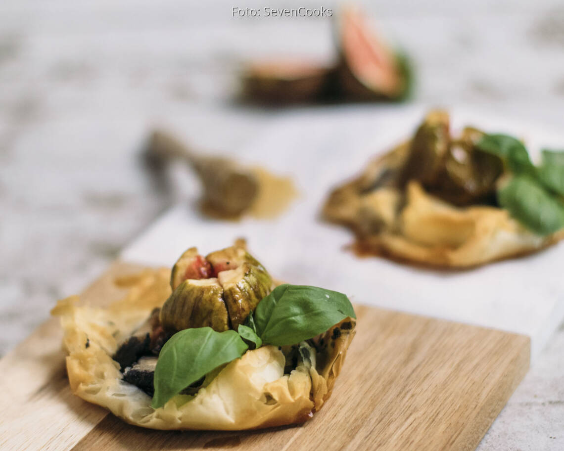 Zwei Asche Käse Tarteletts auf einem Brett mit Honig und Feigen