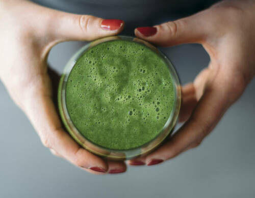 Feldsalatsmoothie in Händen vor dunklem Hintergrund.