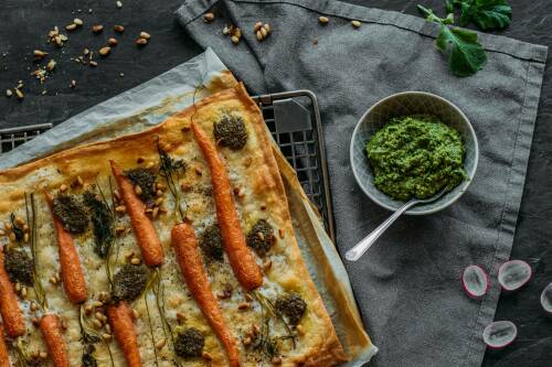 Flammkuchen mit Radieschenpesto und Möhren auf Blech vor dunklem Hintergrund.