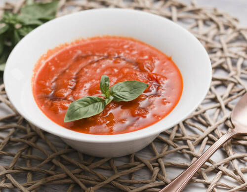 Fruchtige Tomatensuppe in weißem Teller mit Basilikum vor hellem Hintergrund.