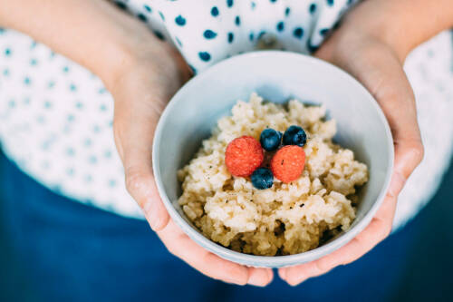 Fruchtiger Kokos-Milchreis in Schüssel und Händen vor hellem Hintergrund.